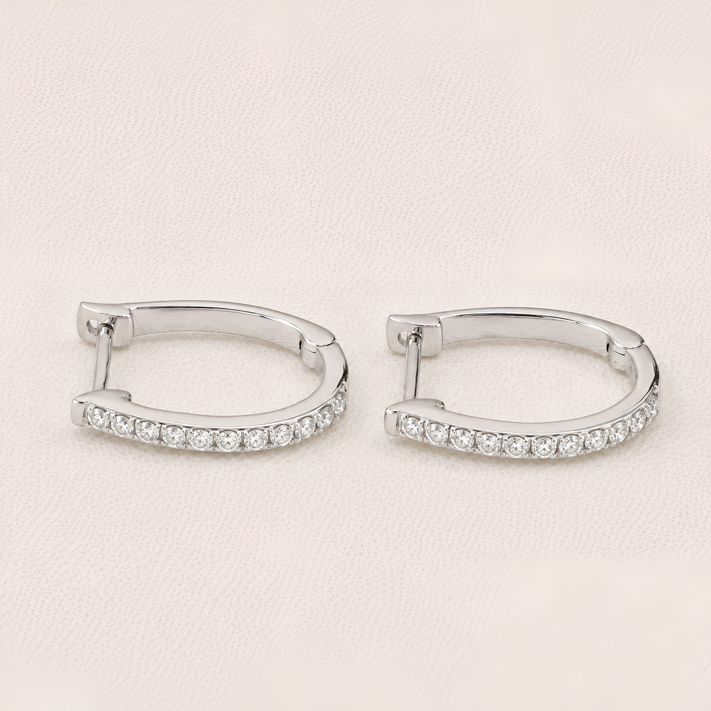 Pair of silver hoop earrings with clear gemstones on a light beige background