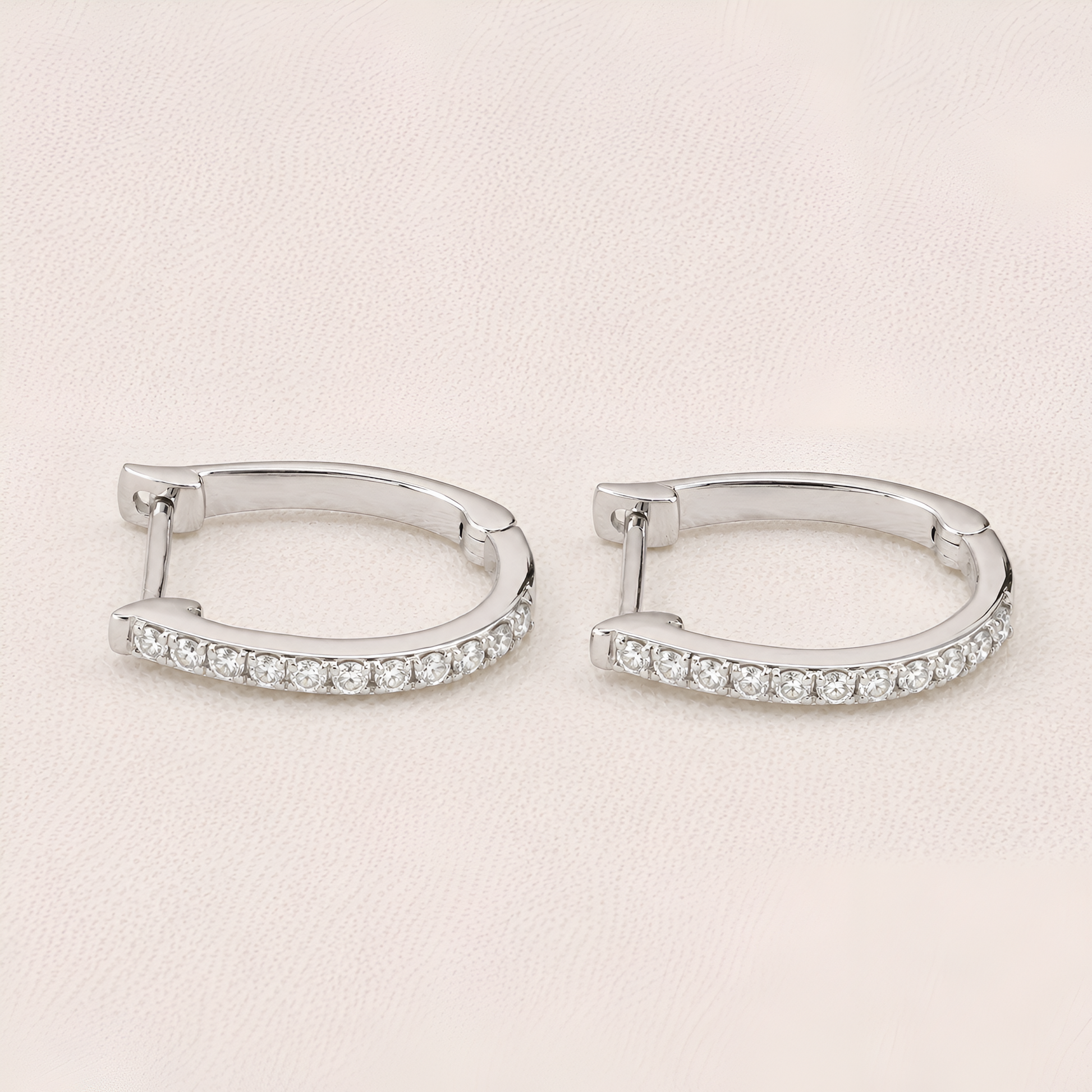 Pair of silver hoop earrings with clear gemstones on a light beige background