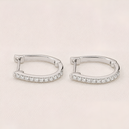 Pair of silver hoop earrings with clear gemstones on a light beige background