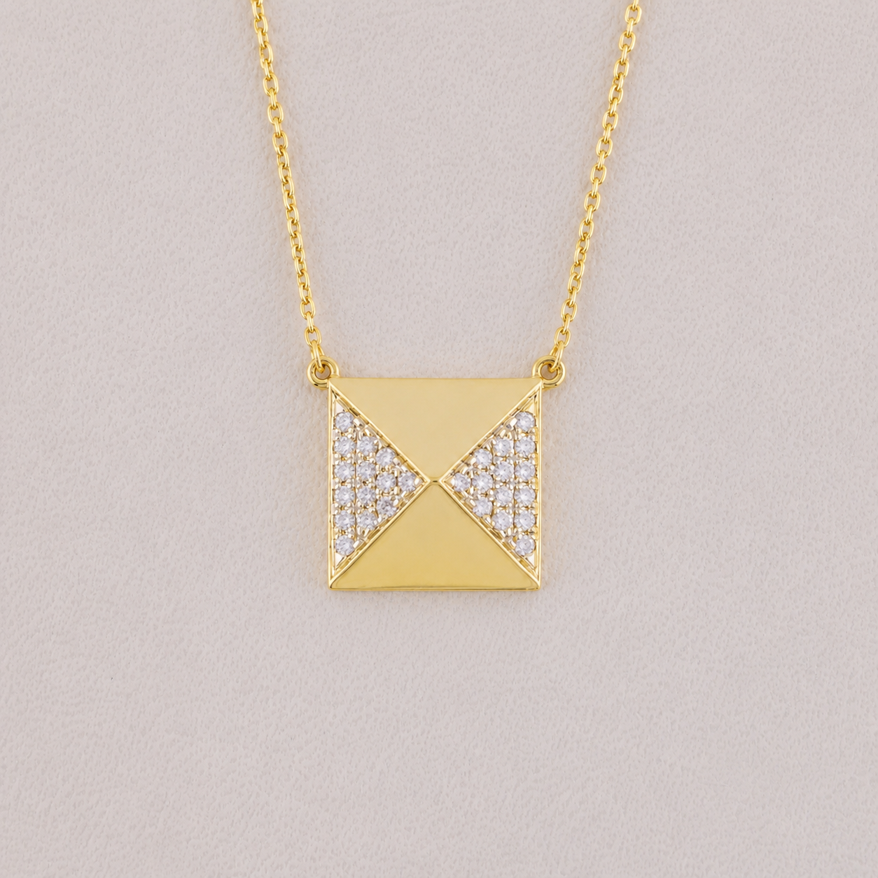 Gold necklace with a square pendant on a light gray background