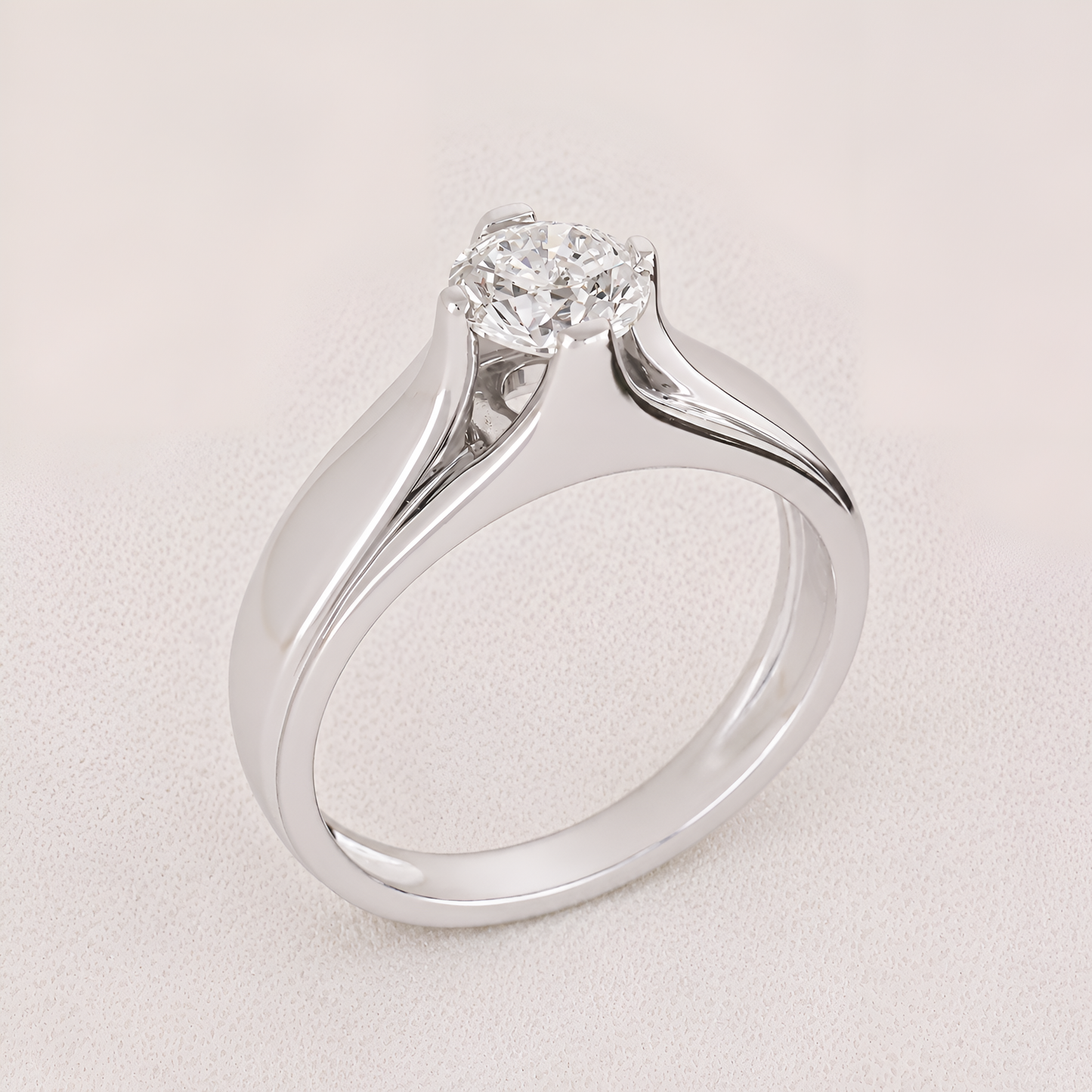 A silver solitaire engagement ring with a round brilliant-cut diamond, set in a polished three-stone band on a textured light beige background.