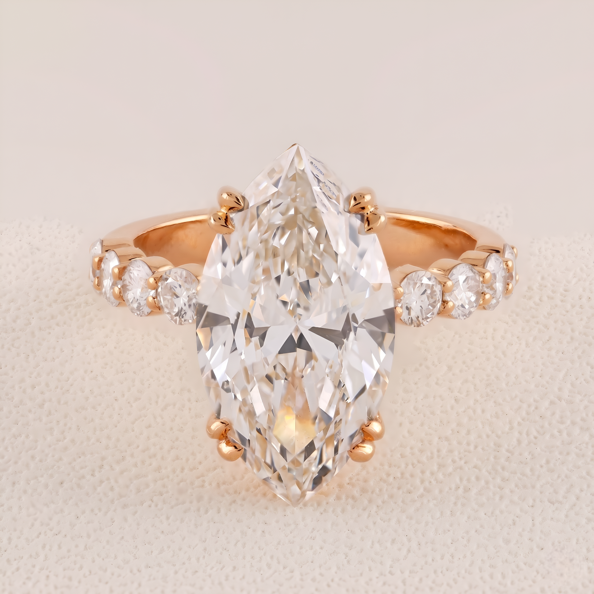 Rose gold ring with a large pear-shaped diamond and smaller diamonds on a beige background