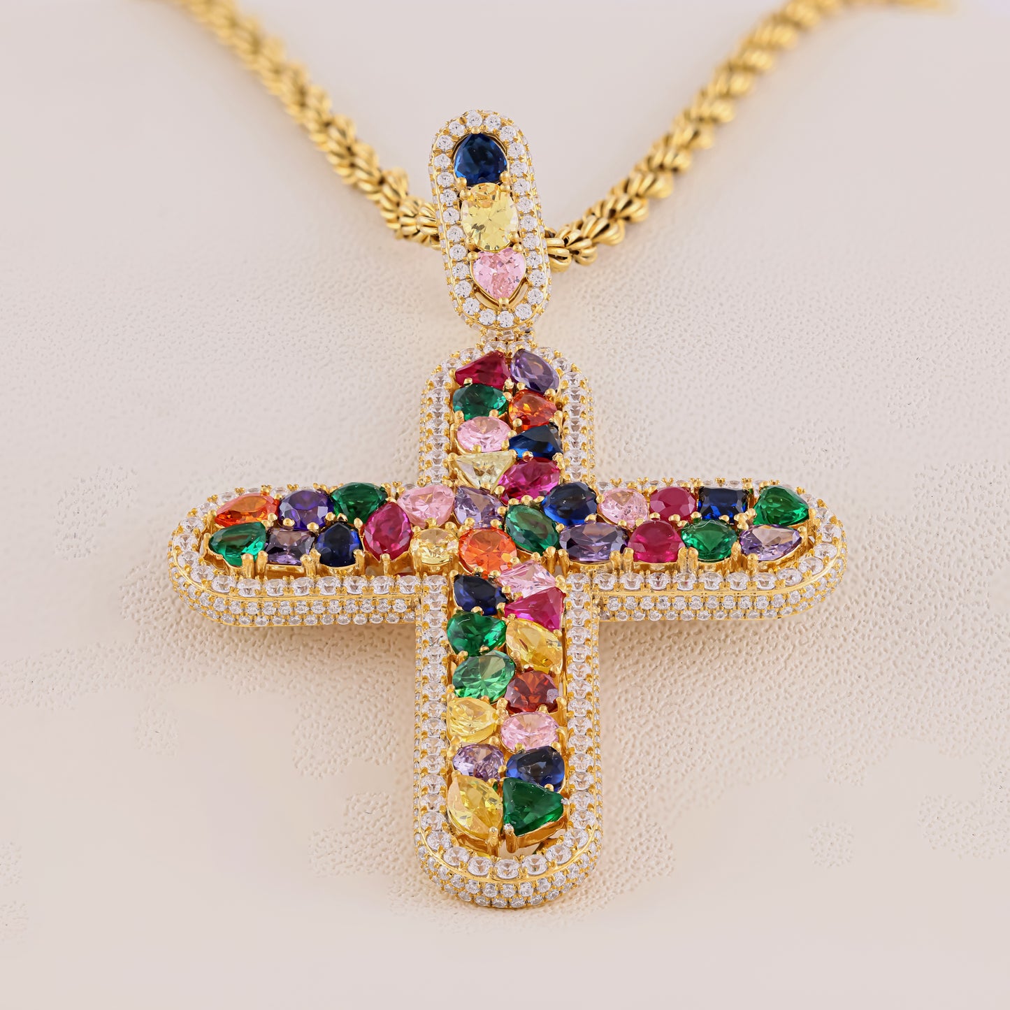Colorful gemstone cross pendant on a gold chain against a beige background
