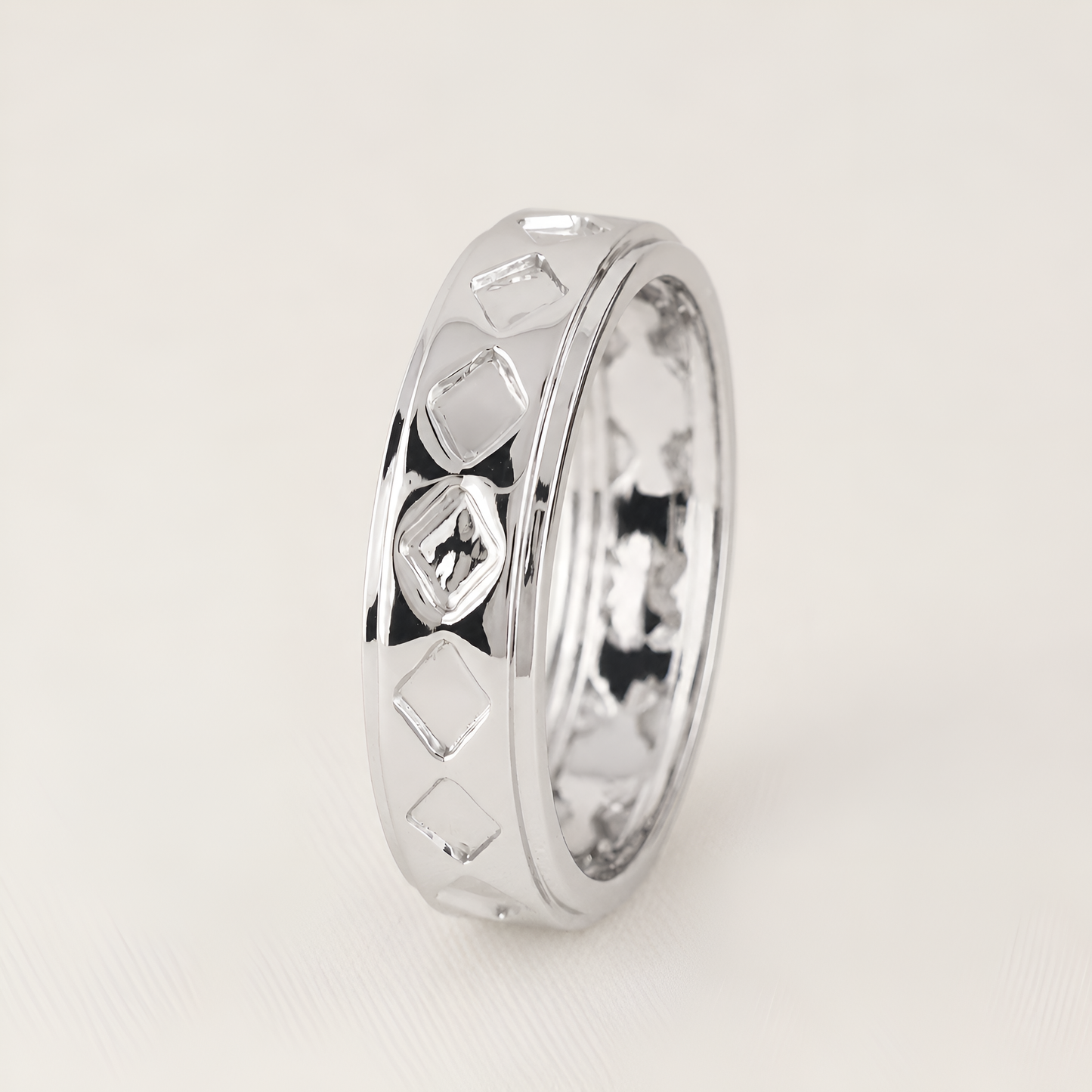 A polished silver ring with a textured geometric diamond pattern on the exterior, standing upright on a light beige background.