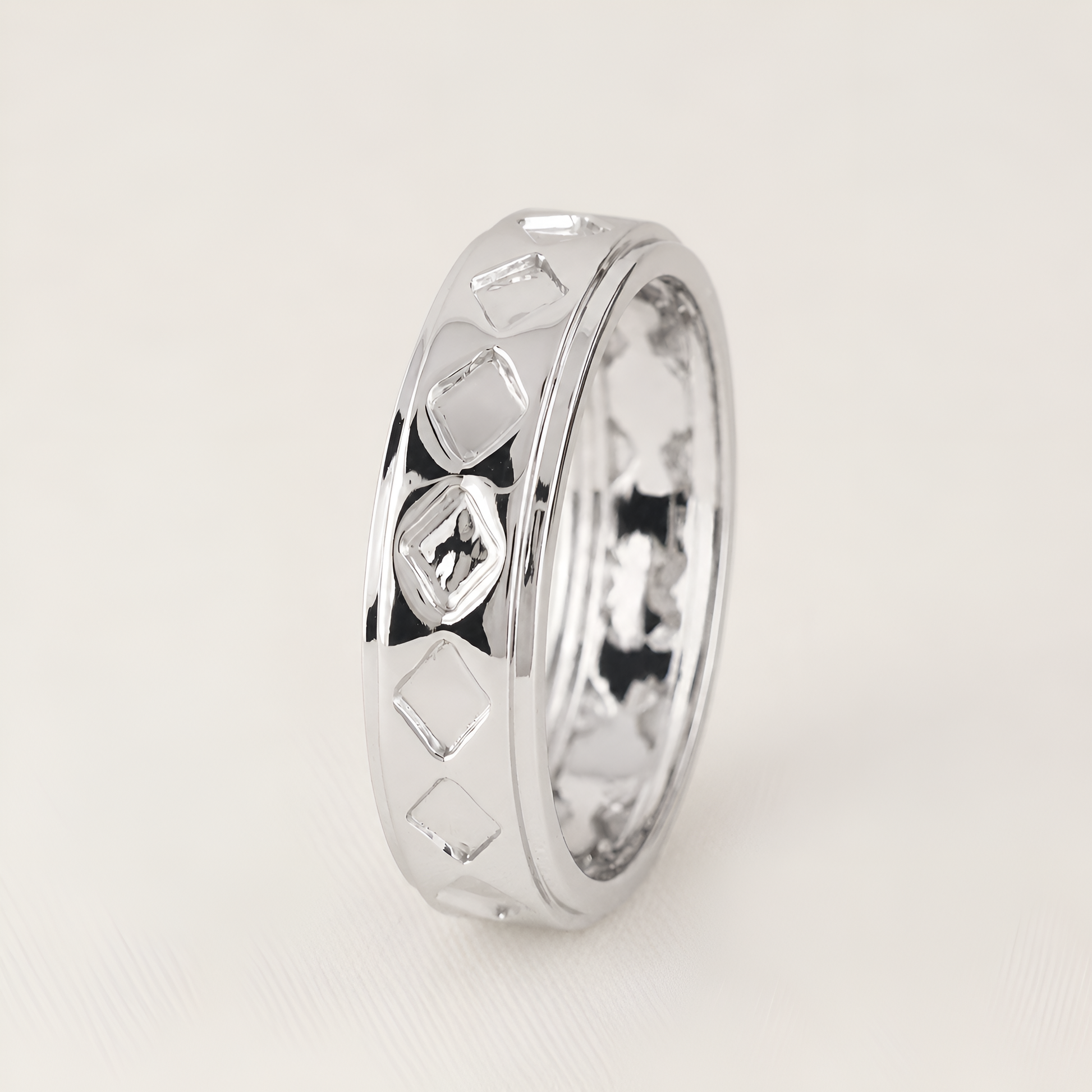 A polished silver ring with a textured geometric diamond pattern on the exterior, standing upright on a light beige background.