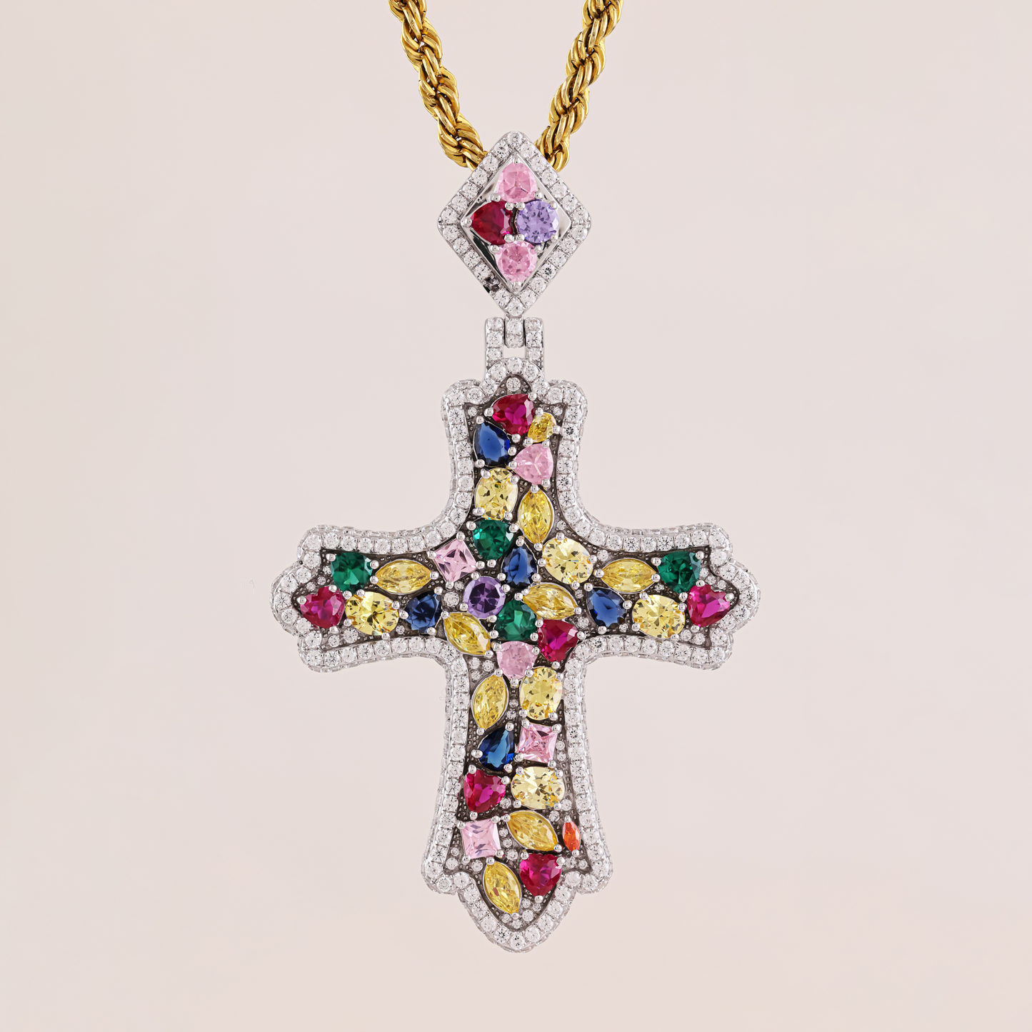 Jeweled cross pendant with colorful gemstones on a gold chain against a beige background