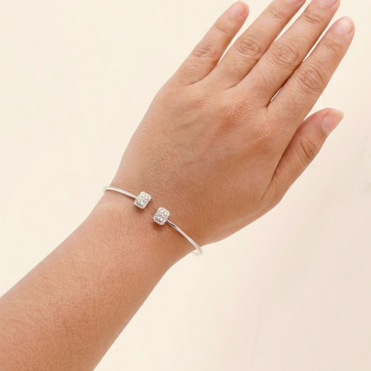 Silver bracelet with two diamond-like charms on a hand against a beige background