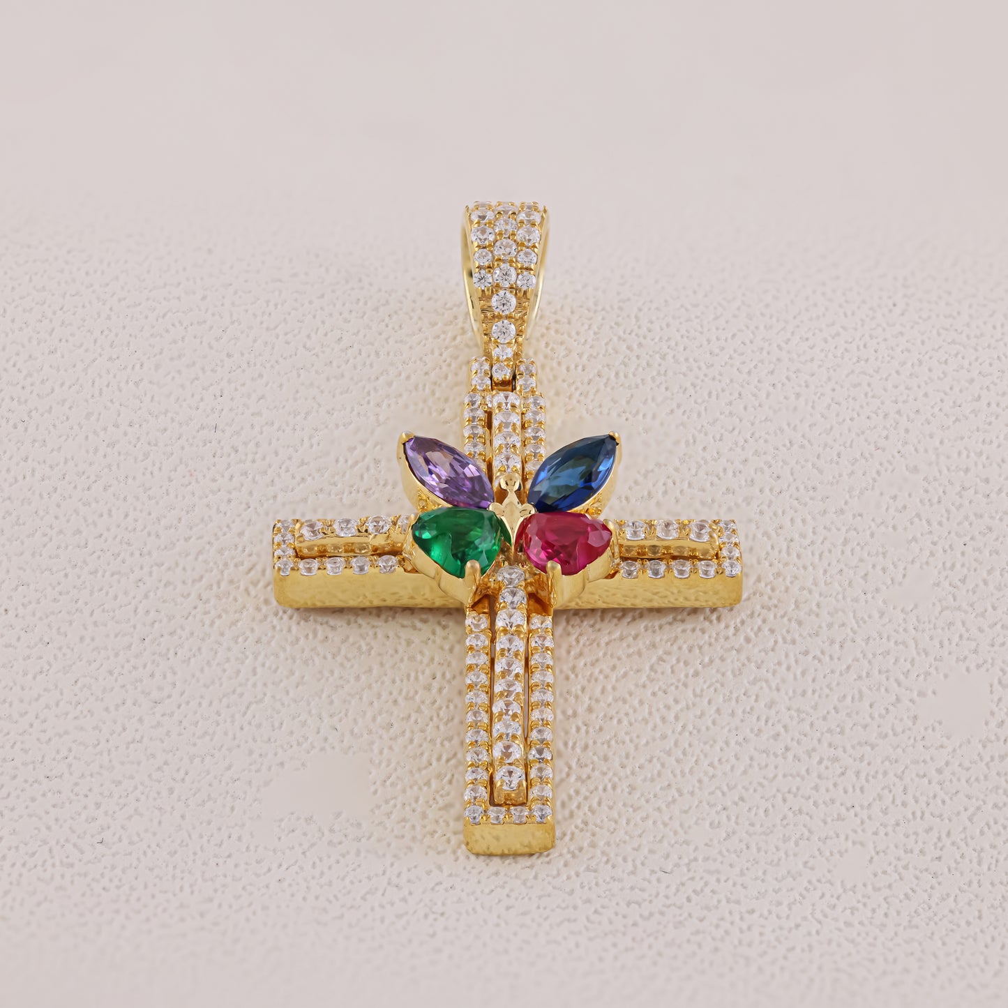 Gold cross pendant with colorful gemstones on a light beige background