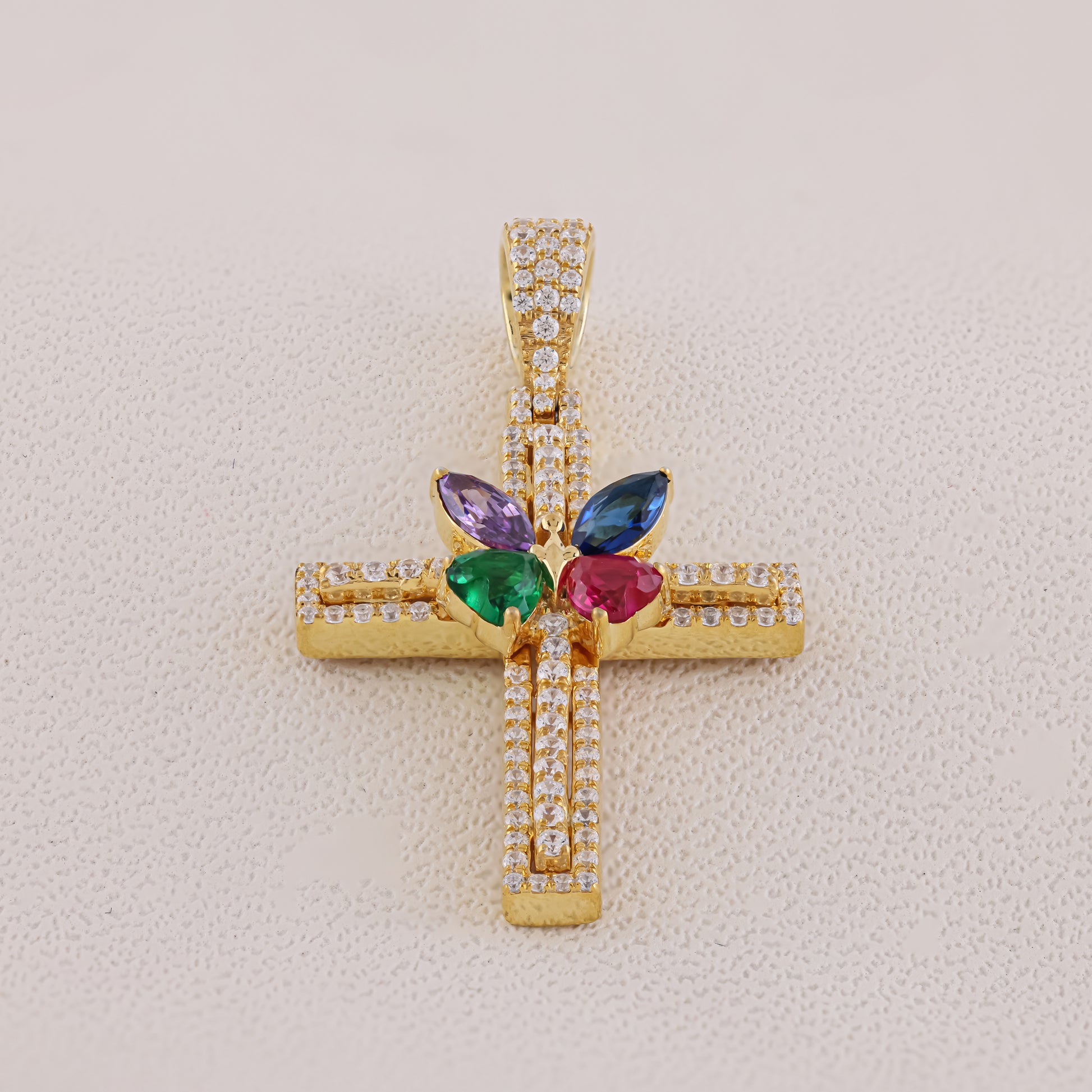 Gold cross pendant with colorful gemstones on a light beige background