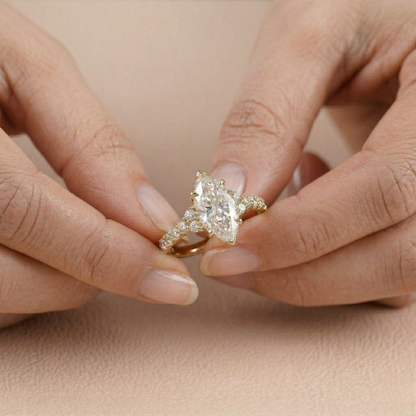Gold ring with a pear-shaped diamond held between two hands on a beige background