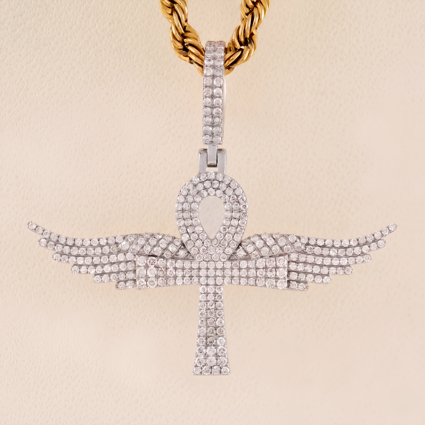 Diamond-studded ankh pendant on a gold chain against a beige background