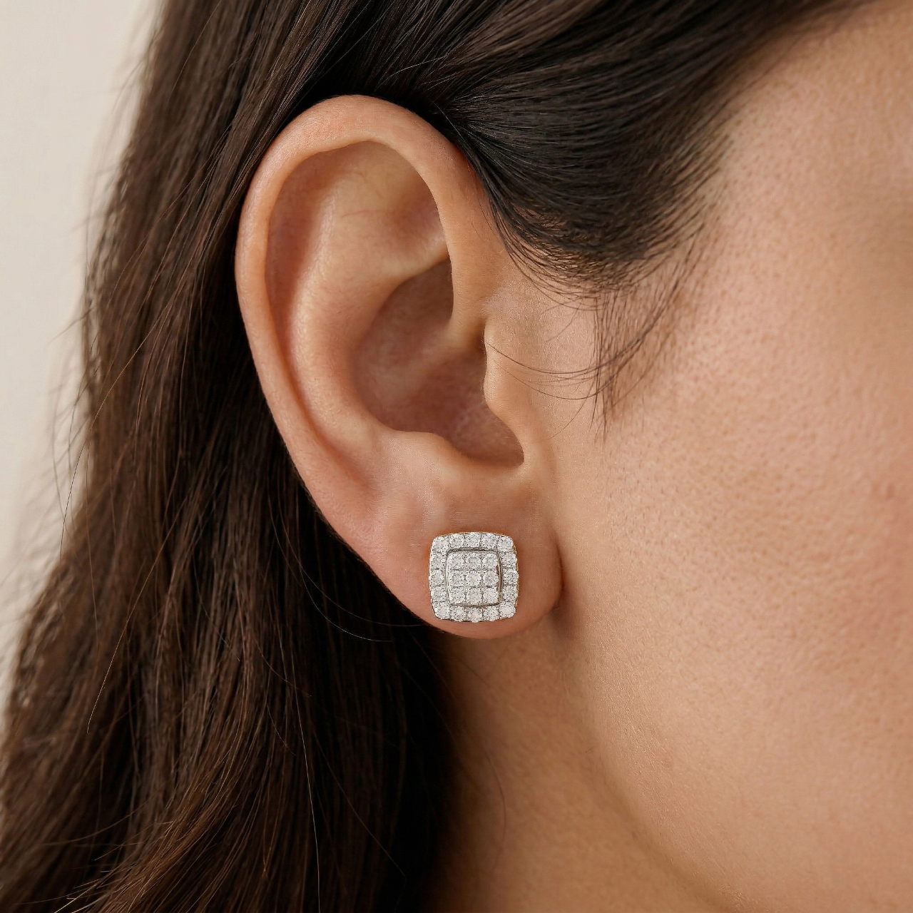 Close-up of an ear wearing a square diamond earring with a neutral background