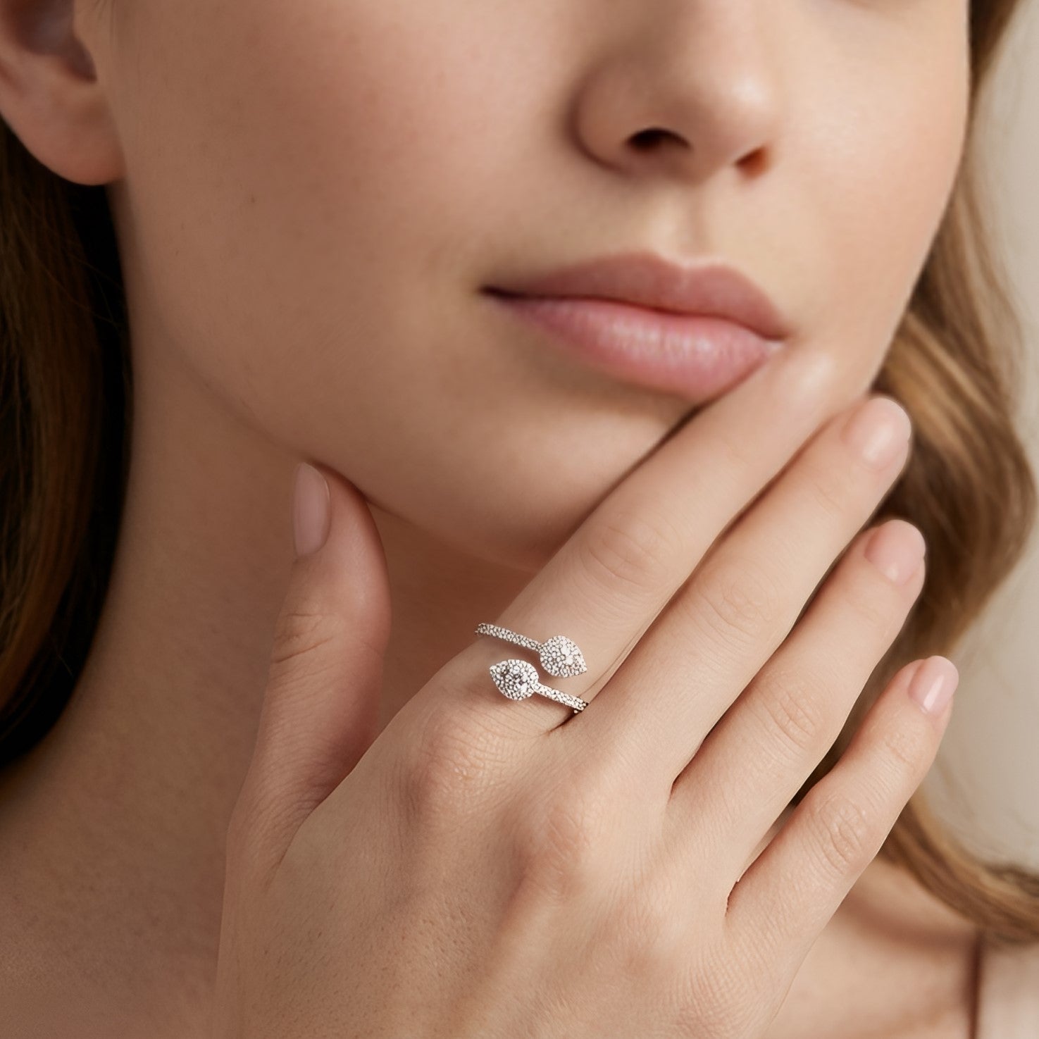 Close-up of a woman's hand wearing a silver ring with a diamond, touching her chin.