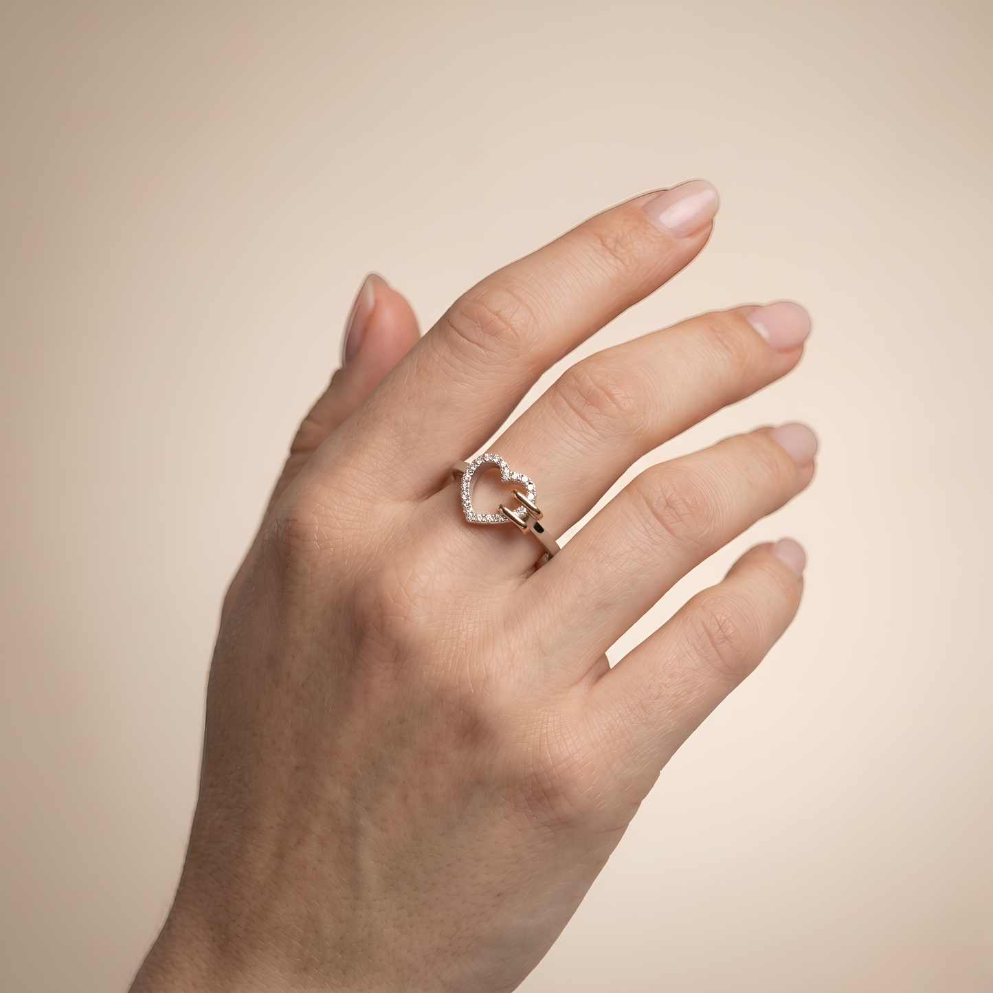 Hand wearing a heart-shaped diamond ring on a beige background