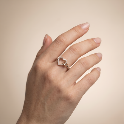 Hand wearing a heart-shaped diamond ring on a beige background
