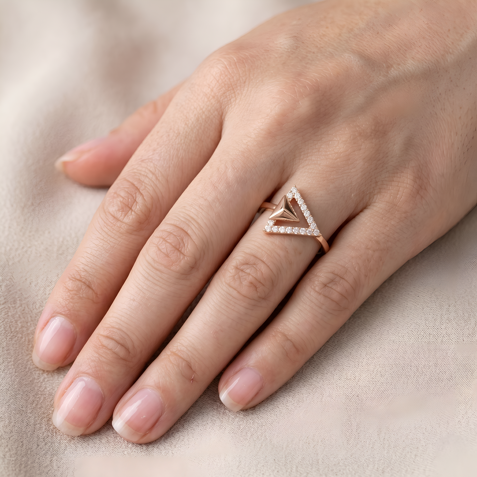 Hand wearing a rose gold triangle-shaped diamond ring on a beige background