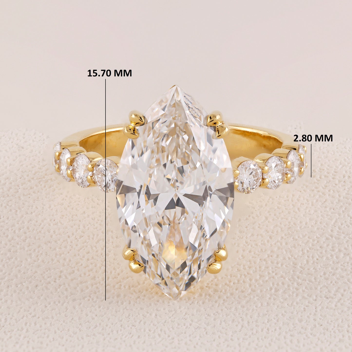 Gold ring with a large pear-shaped diamond and smaller diamonds on a beige background