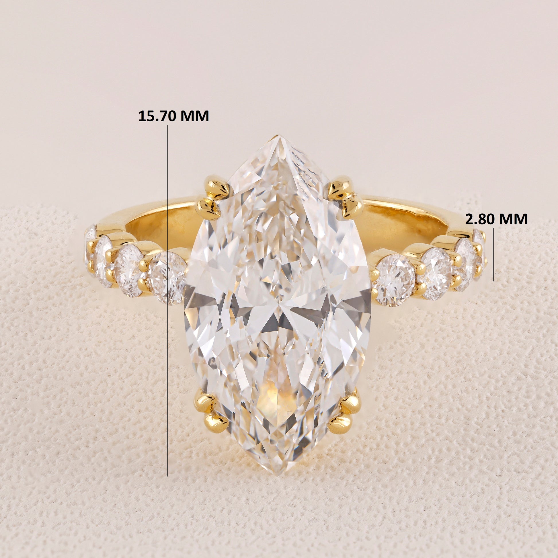 Gold ring with a large pear-shaped diamond and smaller diamonds on a beige background