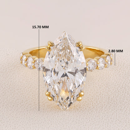 Gold ring with a large pear-shaped diamond and smaller diamonds on a beige background