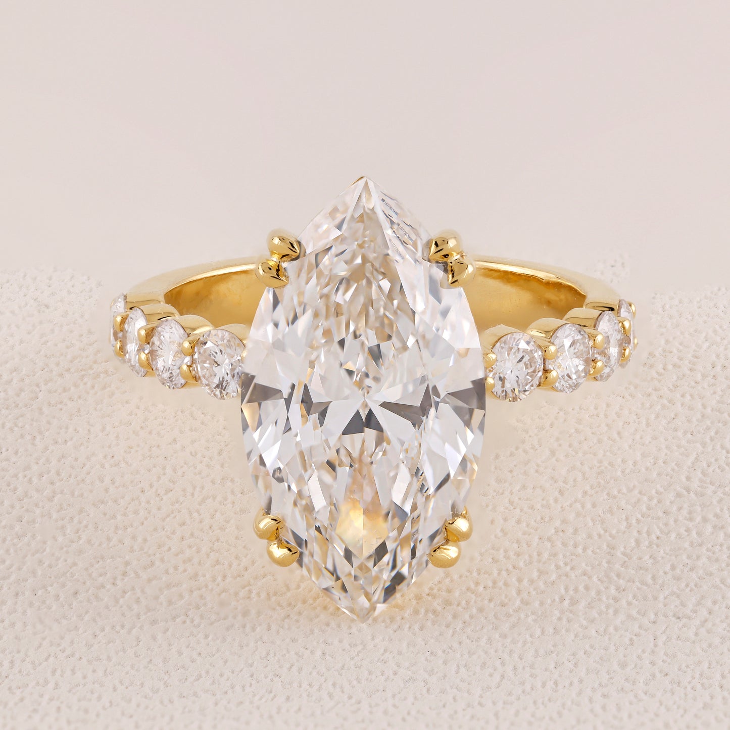 Gold ring with a large pear-shaped diamond and smaller diamonds on a beige background