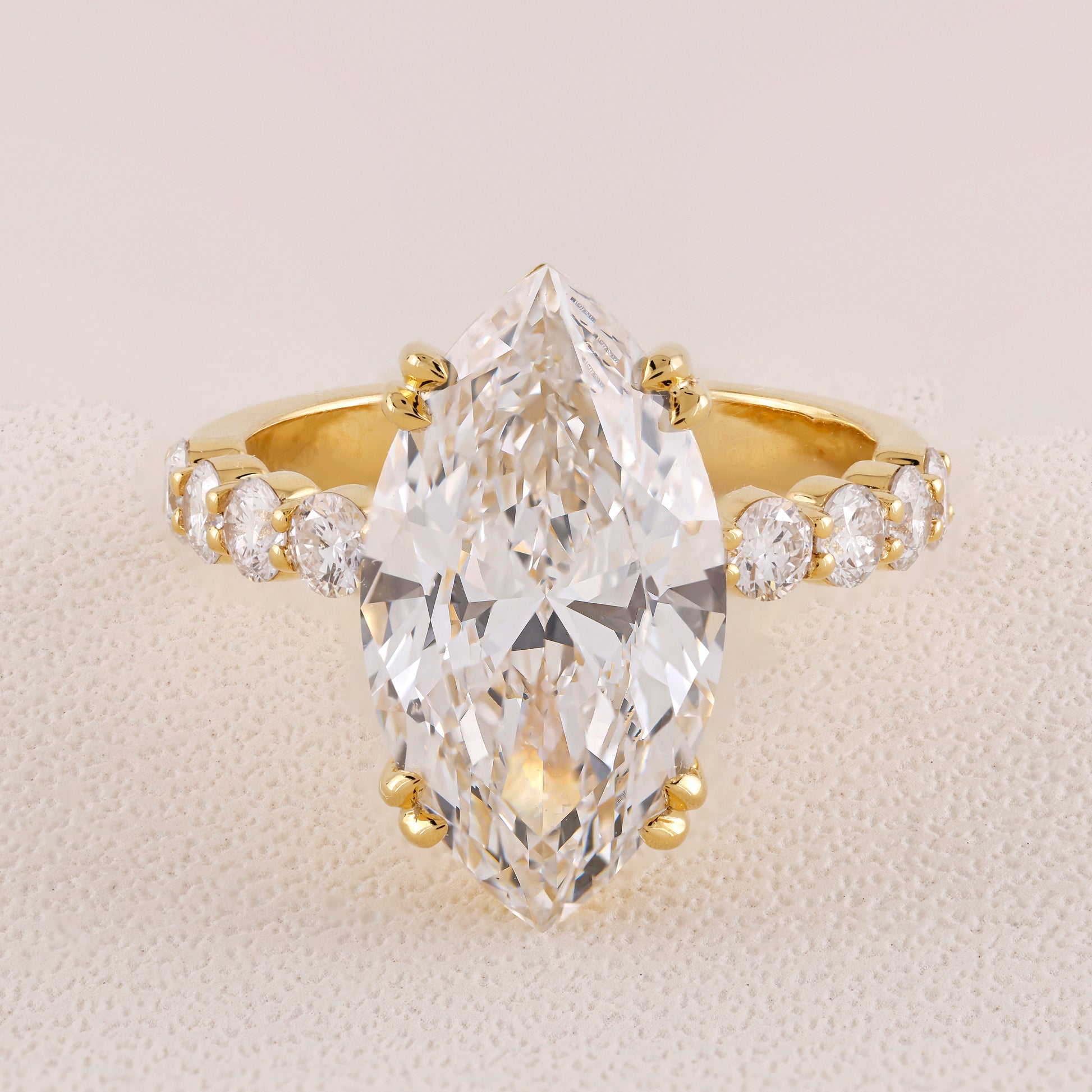 Gold ring with a large pear-shaped diamond and smaller diamonds on a beige background