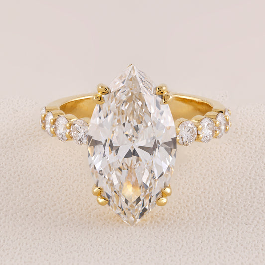 Gold ring with a large pear-shaped diamond and smaller diamonds on a beige background