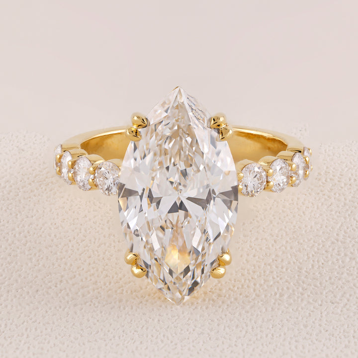 Gold ring with a large pear-shaped diamond and smaller diamonds on a beige background