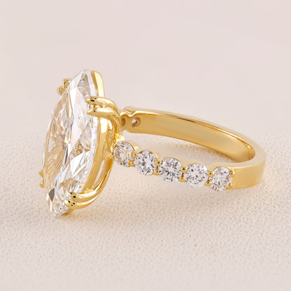 Gold ring with a large diamond and smaller diamonds on the band against a beige background