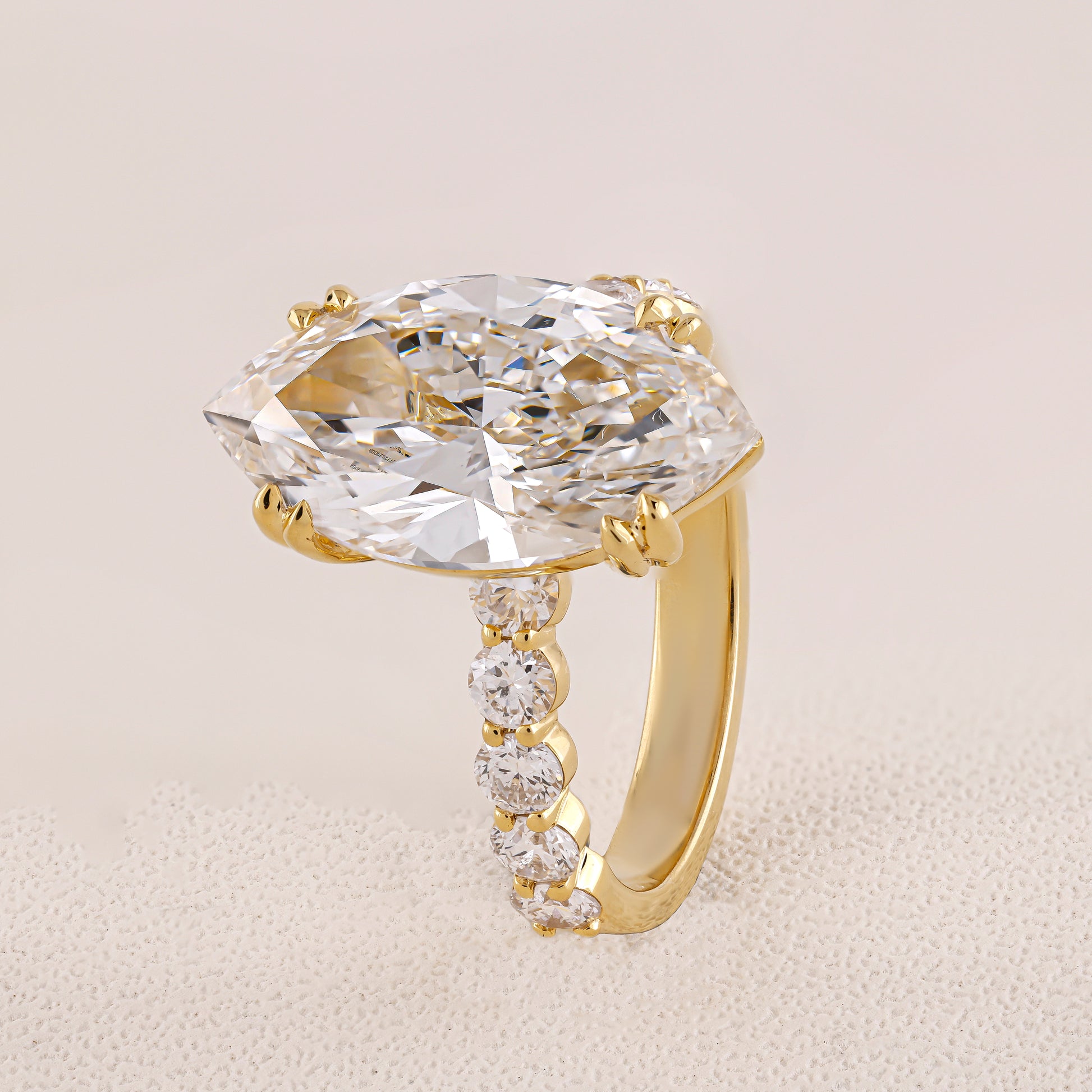 Gold ring with a large diamond and smaller diamonds on the band against a beige background