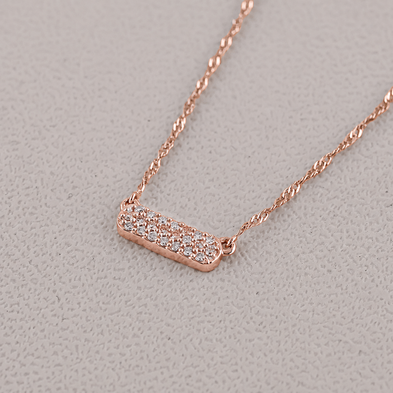 Rose gold necklace with a diamond pendant on a light gray background