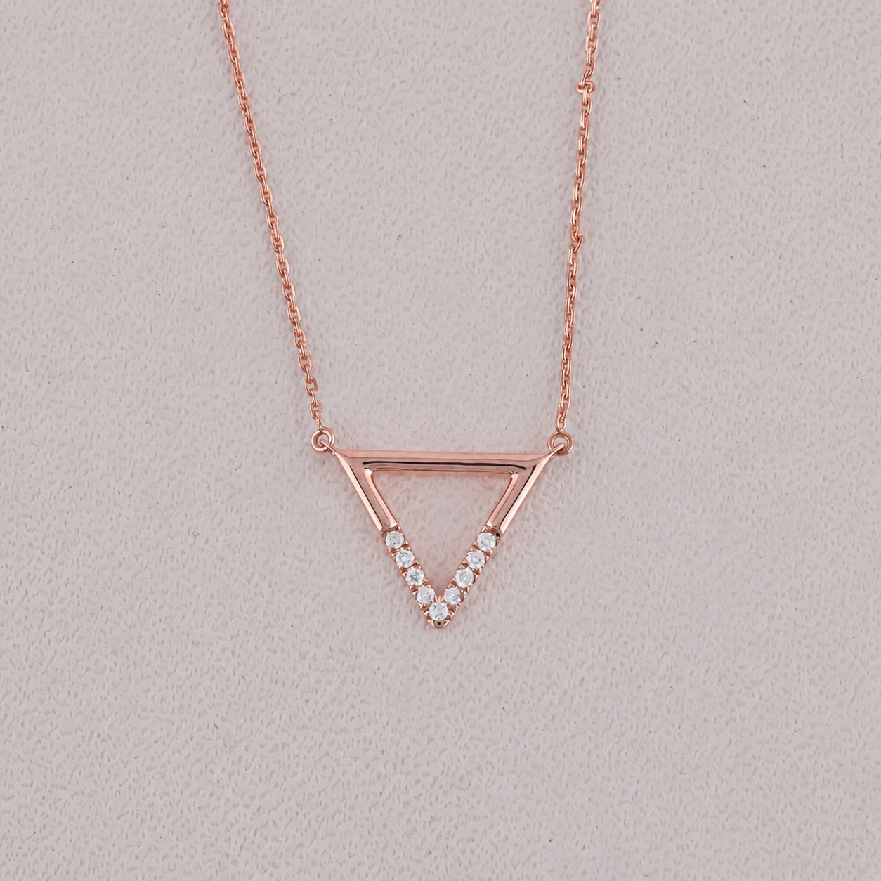 Rose gold triangle necklace with small diamonds on a light gray background