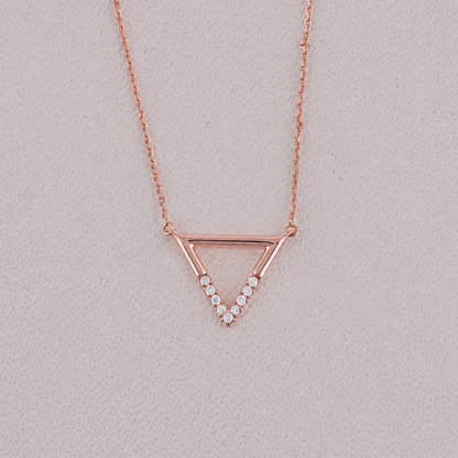 Rose gold triangle necklace with small diamonds on a light gray background