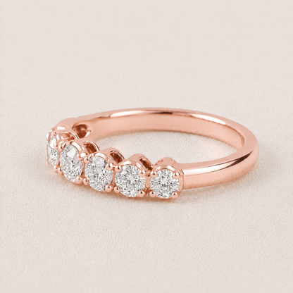 A rose gold diamond ring with five round-cut diamonds set in a row on a polished band, shown on a light beige textured background.