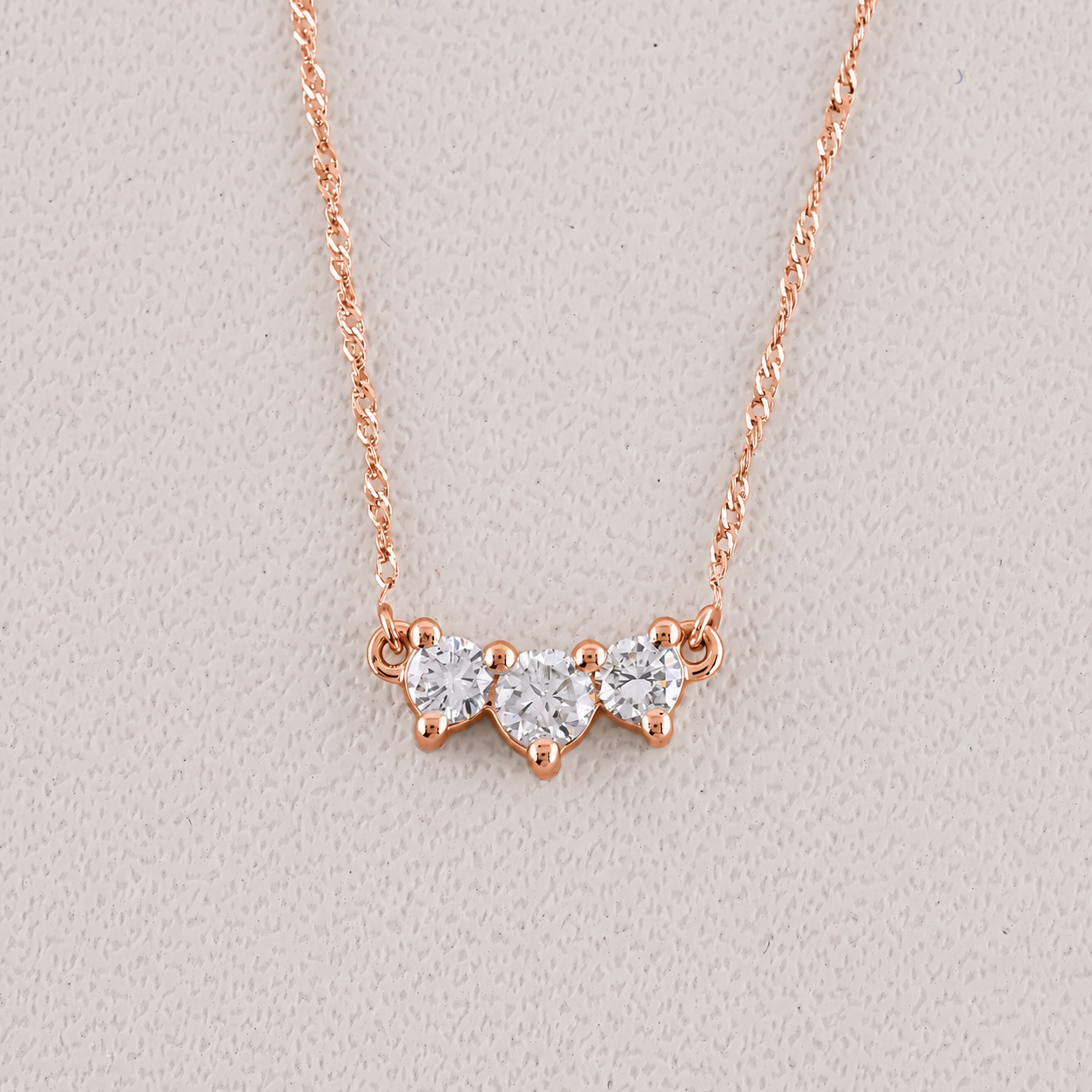 Rose gold necklace with three heart-shaped diamond pendants on a light gray background