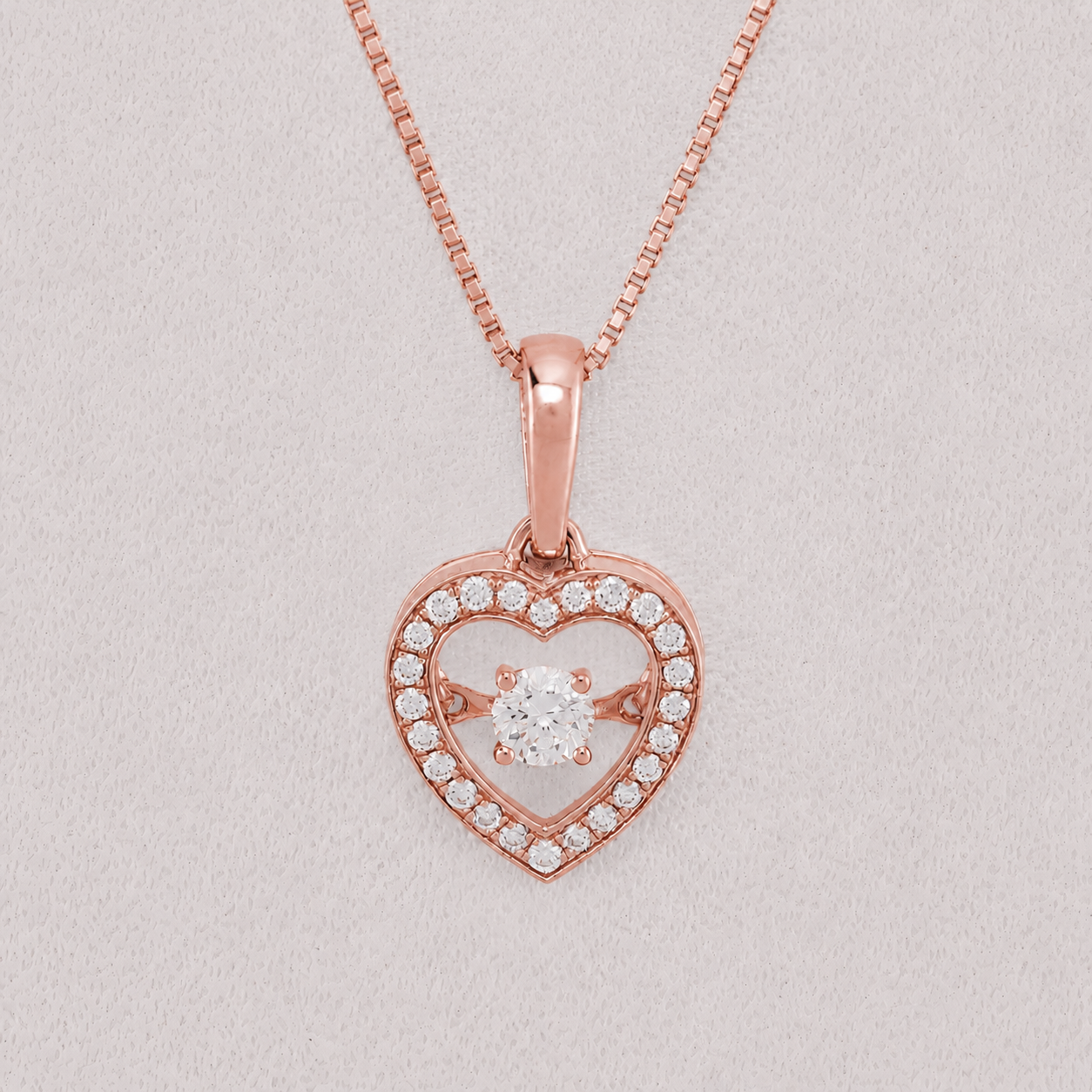 Rose gold heart pendant necklace with a central round-cut clear gemstone and a halo of small clear stones, shown on a matching chain against a light gray background.