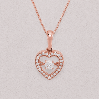Rose gold heart pendant necklace with a central round-cut clear gemstone and a halo of small clear stones, shown on a matching chain against a light gray background.