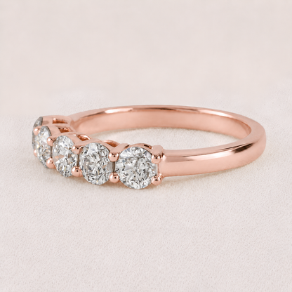 A rose gold five-stone diamond ring with round-cut diamonds set in a polished band, photographed on a soft, light beige textured background.