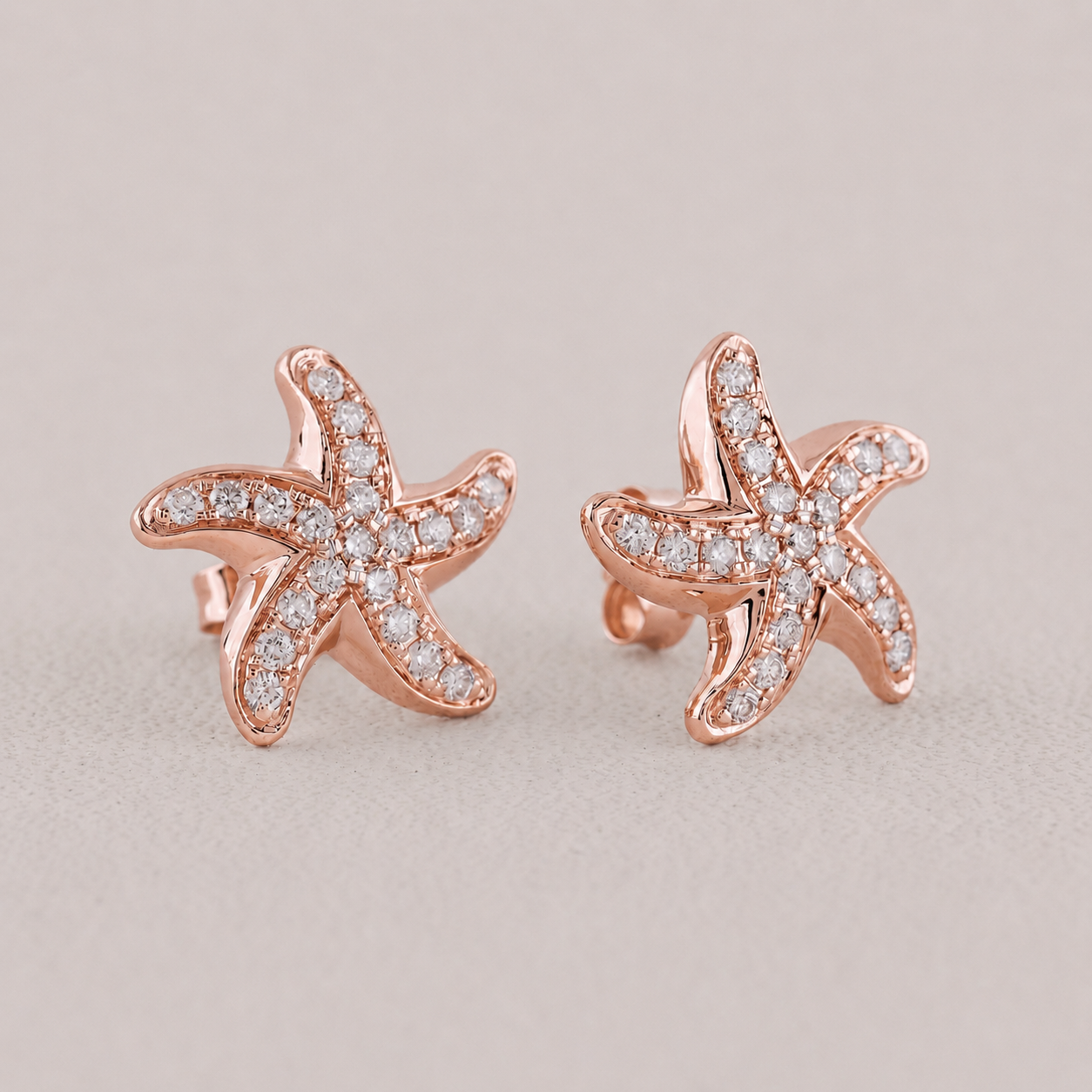 Rose gold starfish earrings with diamond accents on a light gray background
