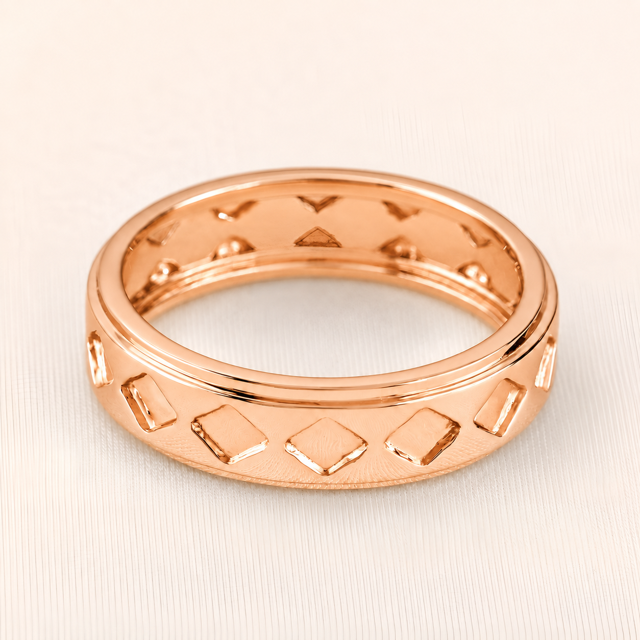 A rose gold band ring with a textured geometric pattern of raised and recessed diamond shapes, shown on a light beige textured background.