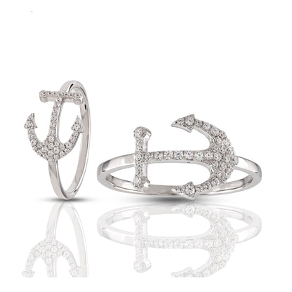 A silver ring in the shape of an anchor, adorned with round-cut cubic zirconia, displayed on a reflective surface.
