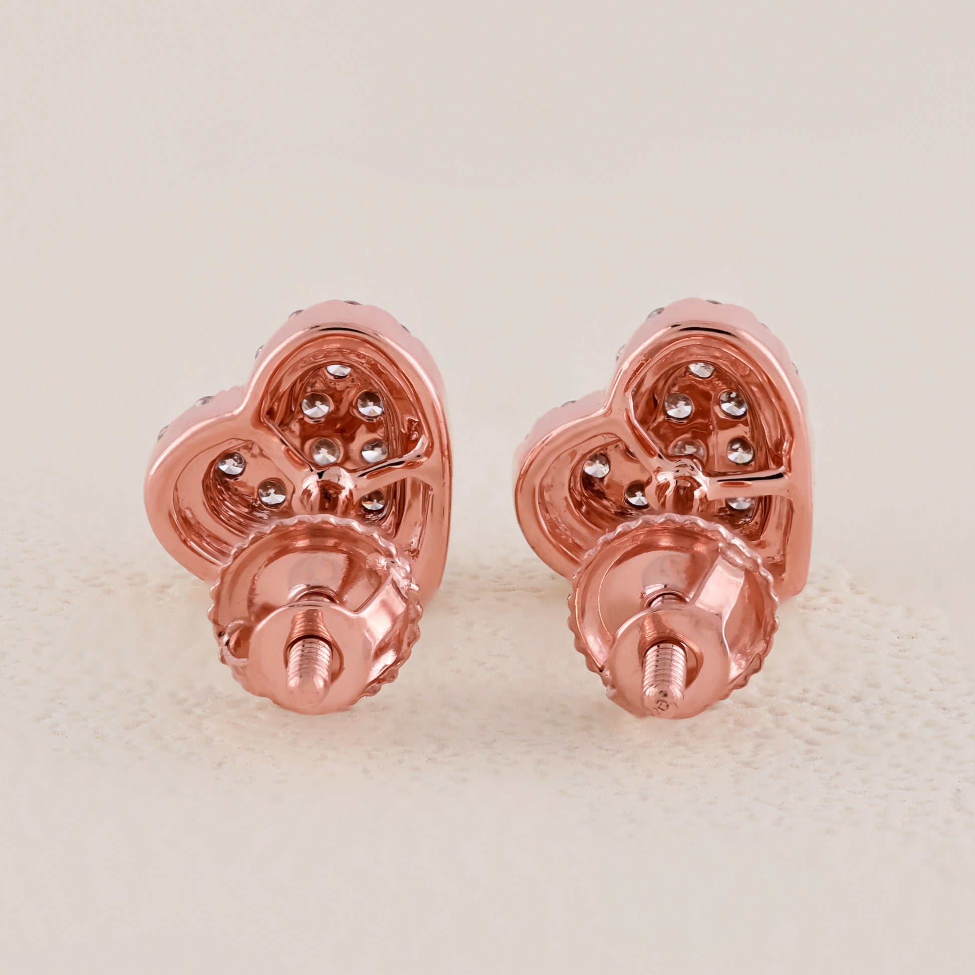 Rose gold heart-shaped earrings with embedded stones on a light beige background