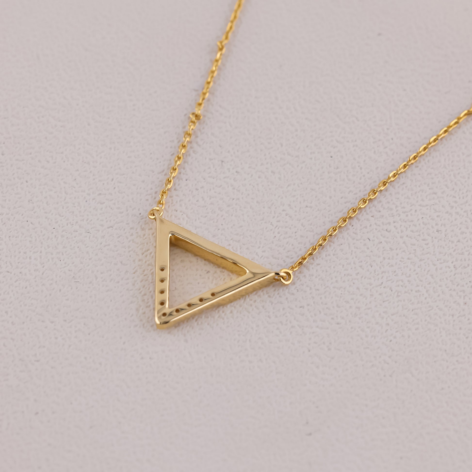 Gold triangle pendant necklace on a light gray background