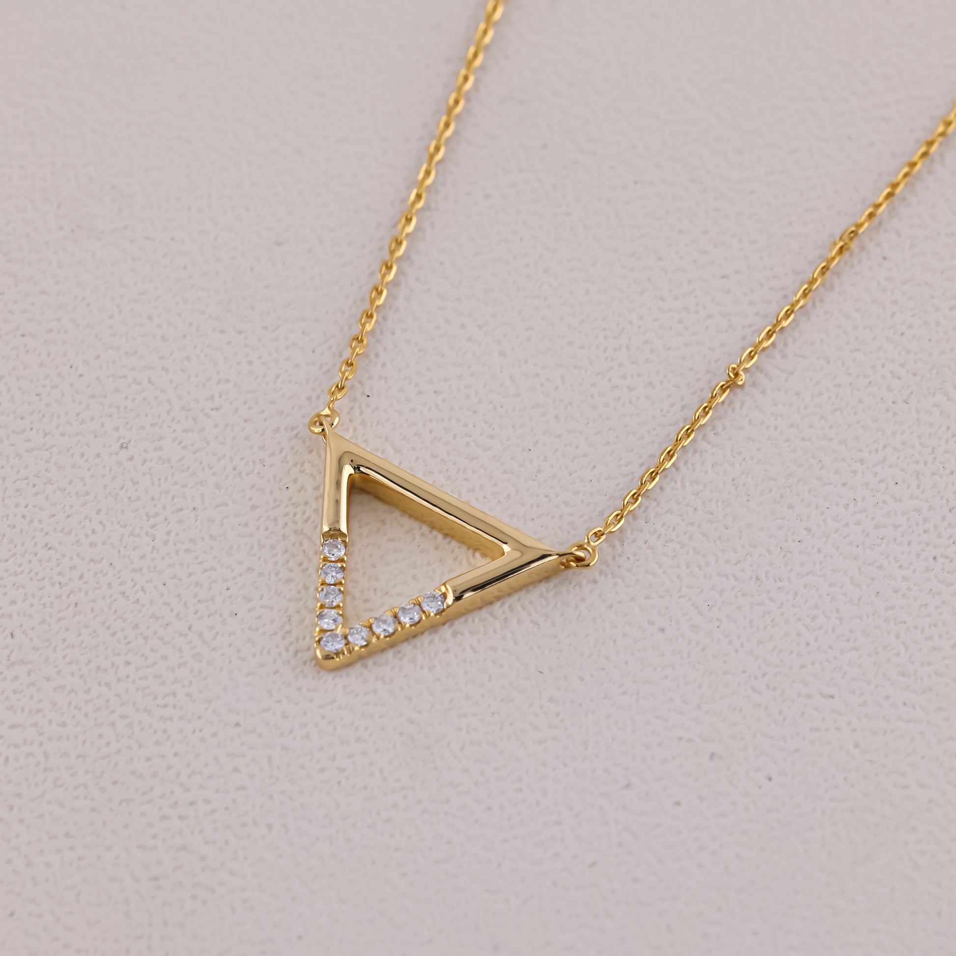 Gold triangle-shaped necklace with embedded stones on a light gray background