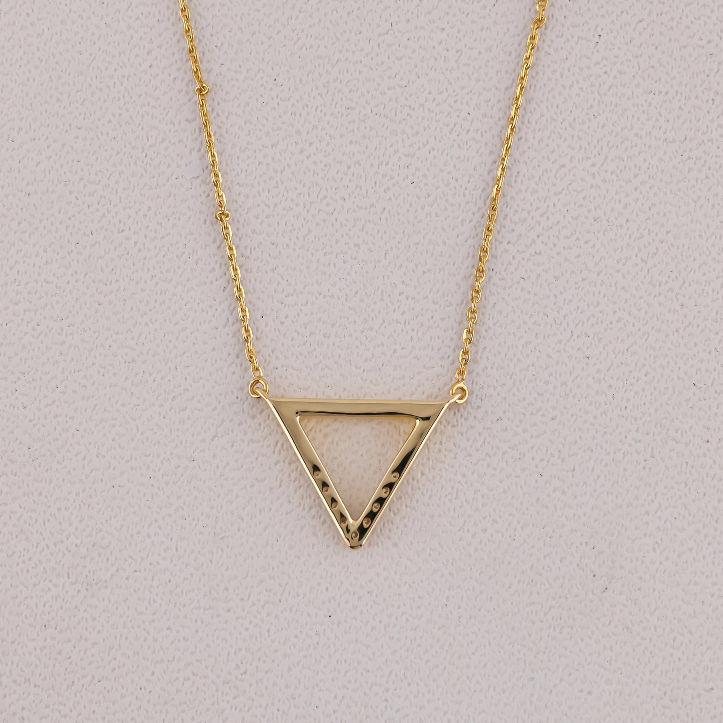 Gold triangle pendant necklace on a light gray background