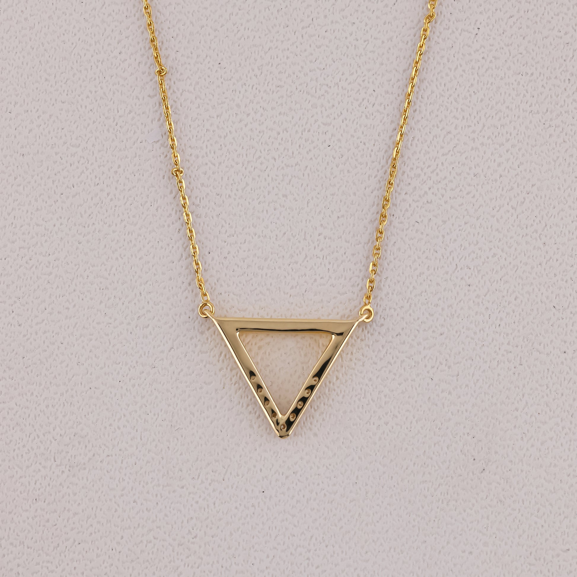 Gold triangle pendant necklace on a light gray background