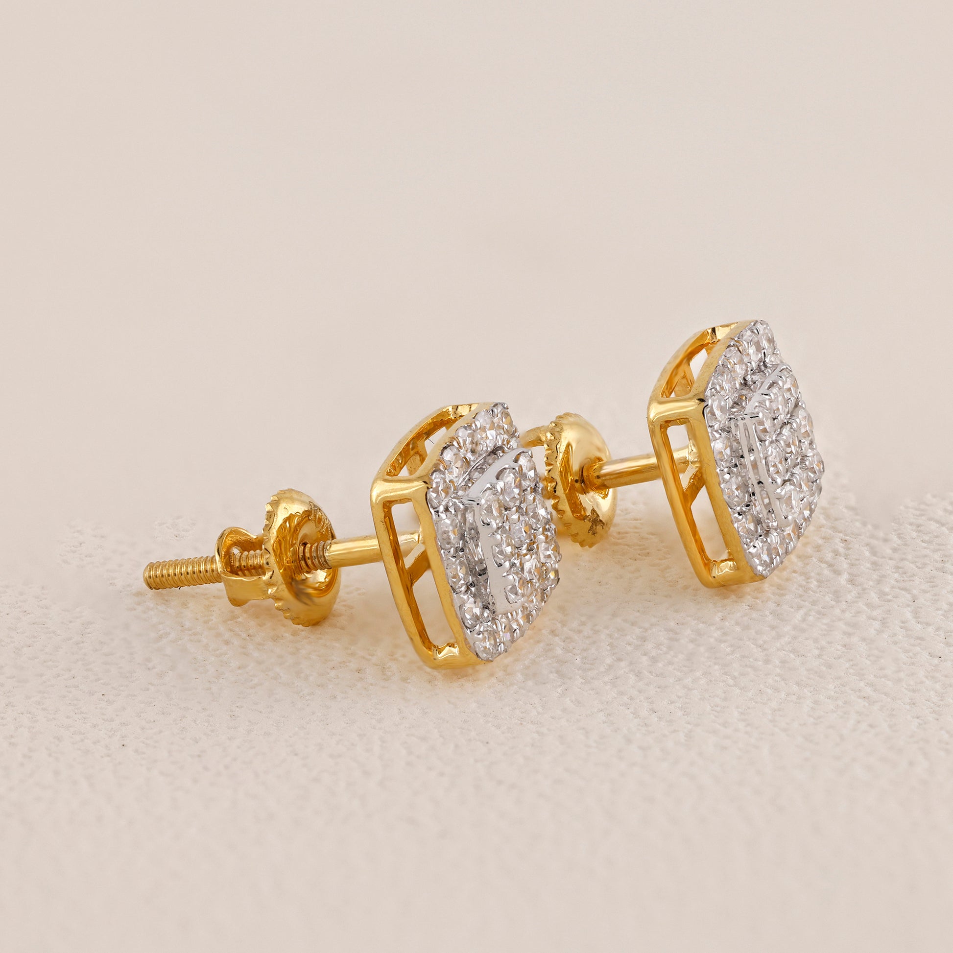 Gold earrings with diamond accents on a light beige background