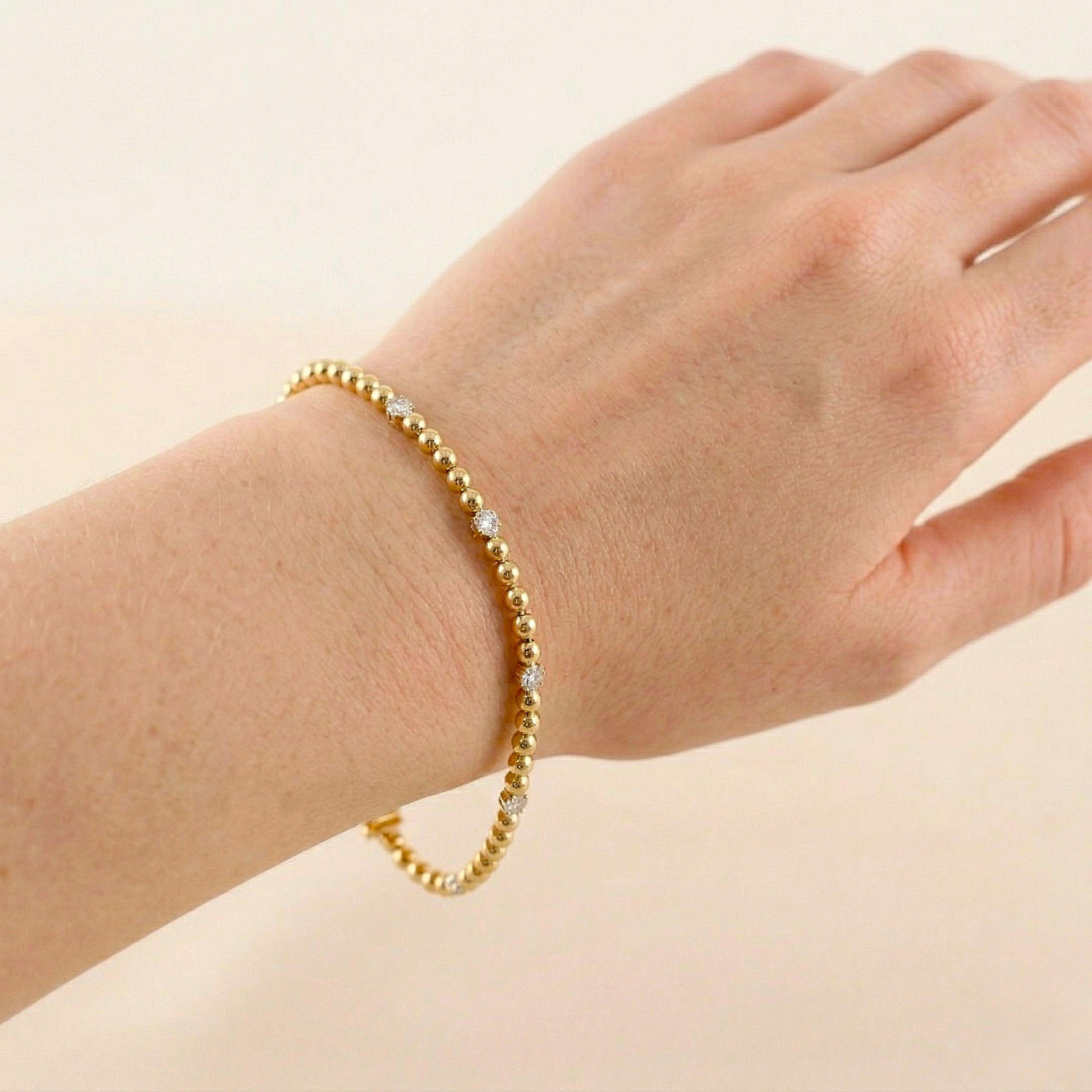Gold beaded bracelet on a wrist against a beige background