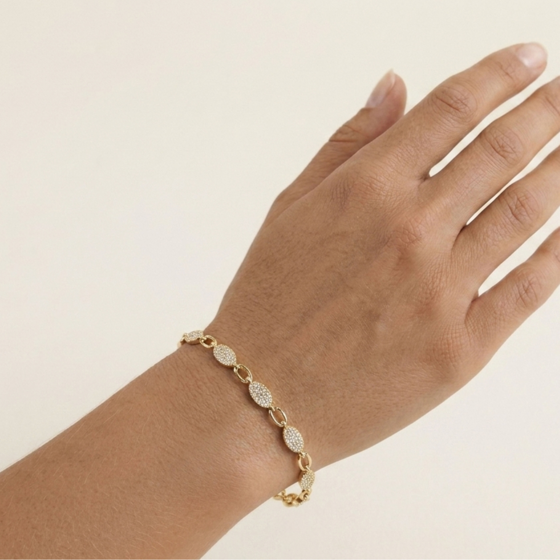 Gold bracelet on a hand against a beige background