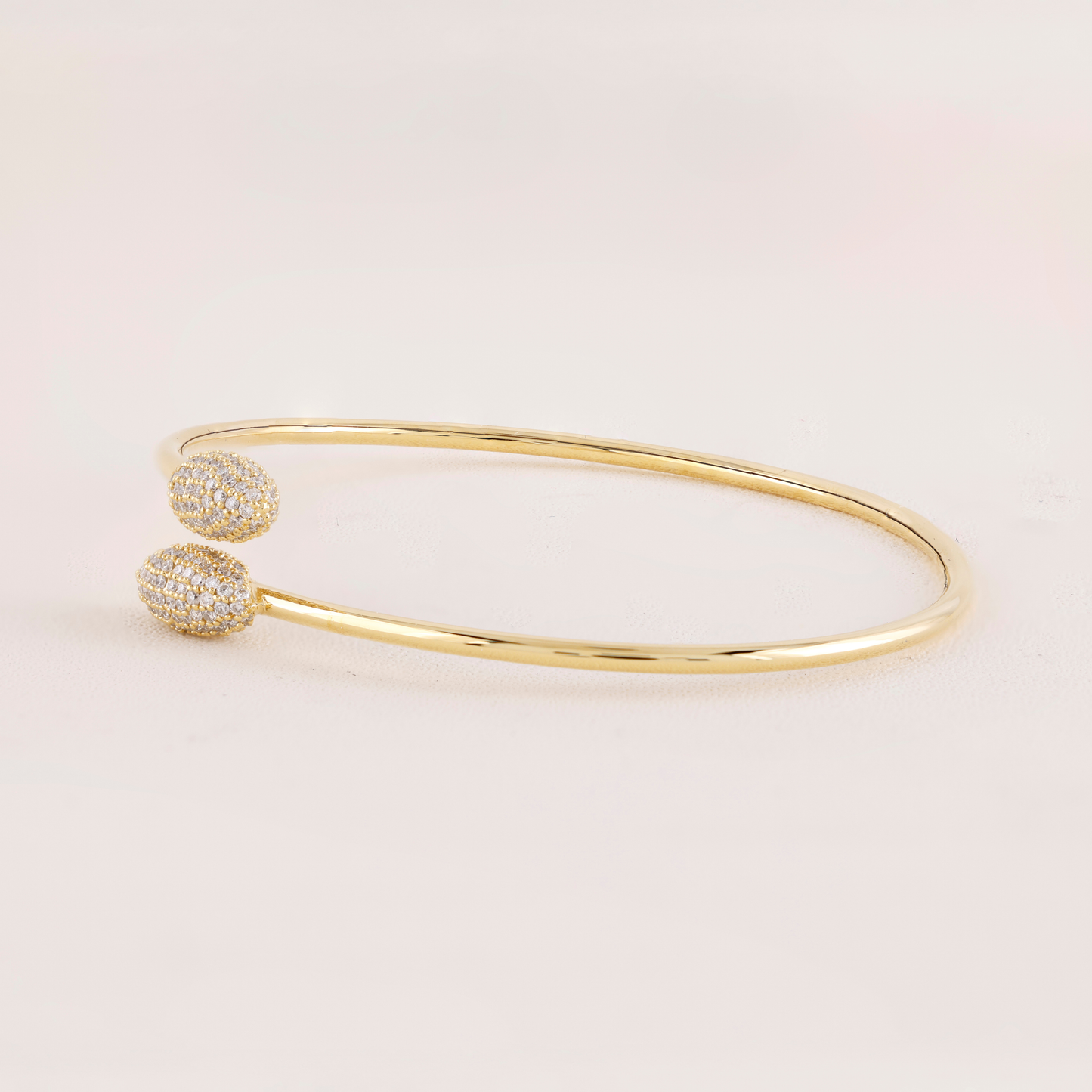 Gold bangle with two diamond-studded ends on a light pink background