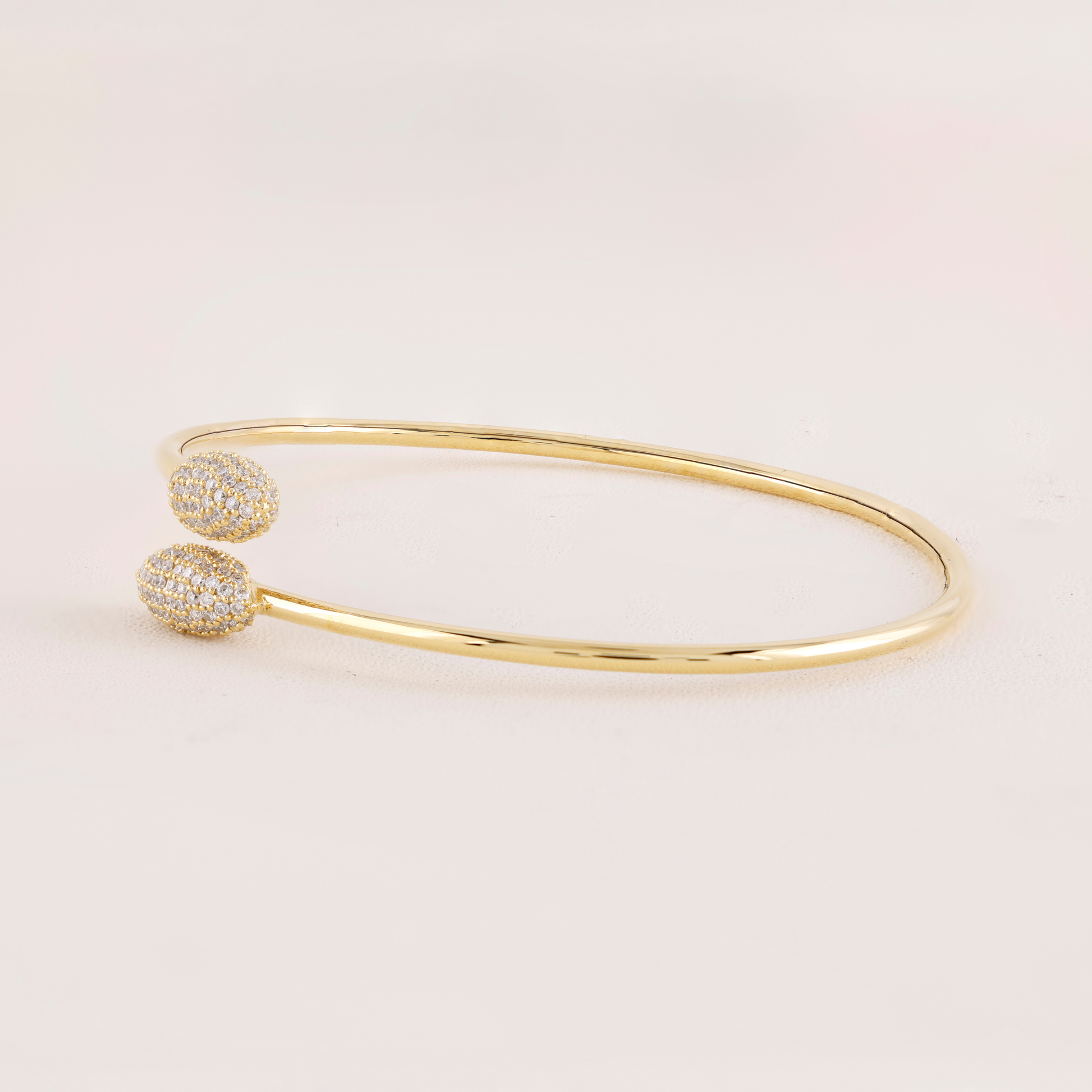 Gold bangle with two diamond-studded ends on a light pink background